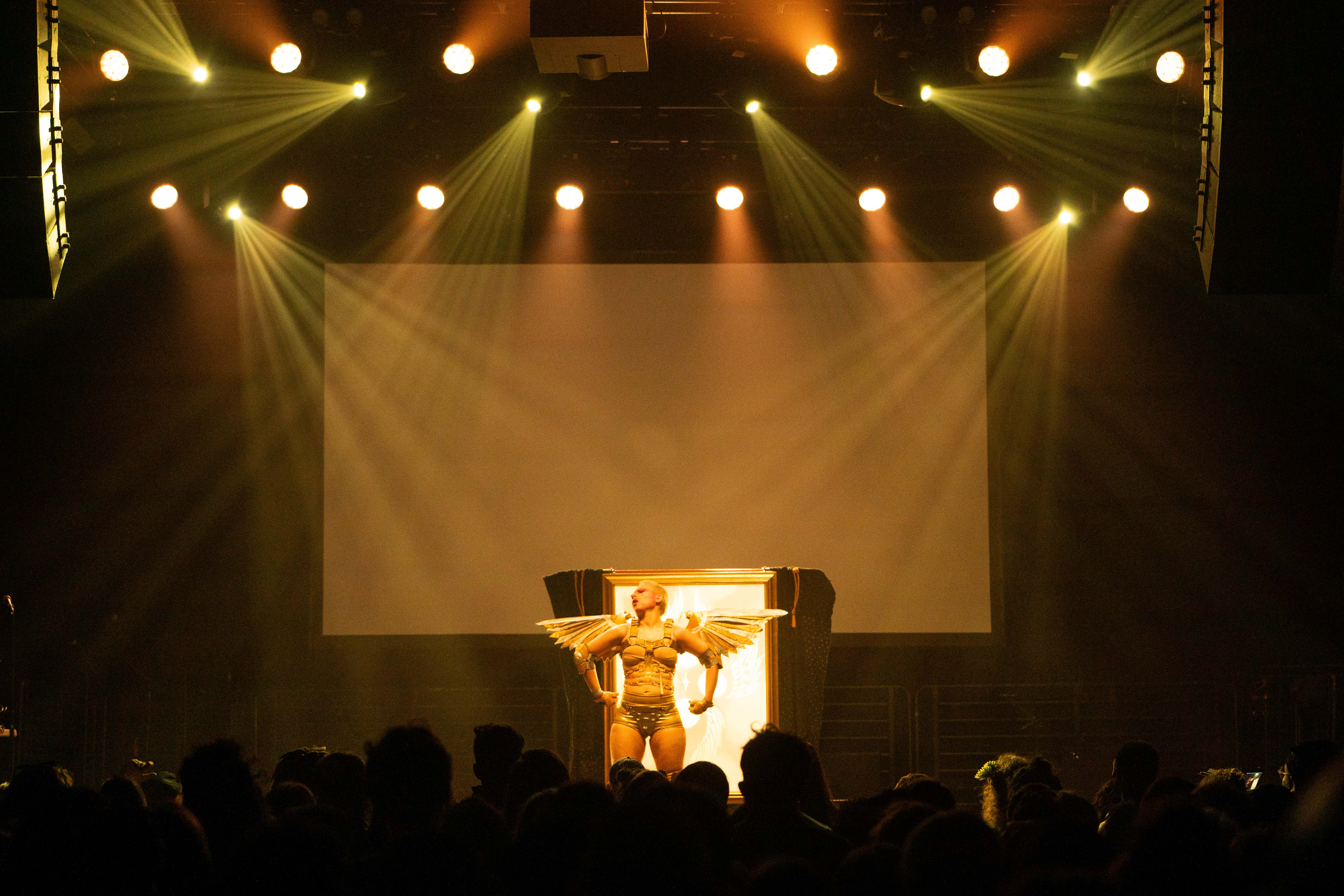 Xtian Mingle onstage in a gold and silver costume with fully outstretched wings.